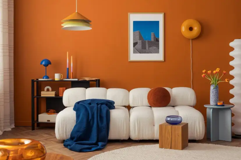 Nowoczesny salon z białą kanapą, pomarańczową ścianą i kolorowymi dodatkami.