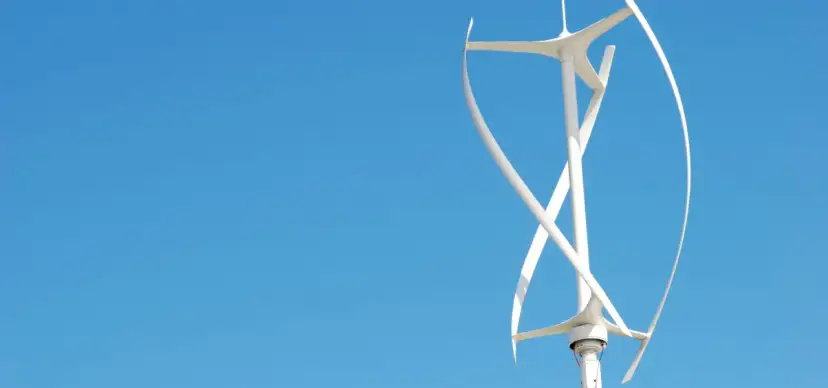 Biały wiatrak na dachu, z zakrzywionymi łopatami, obraca się na tle błękitnego nieba.