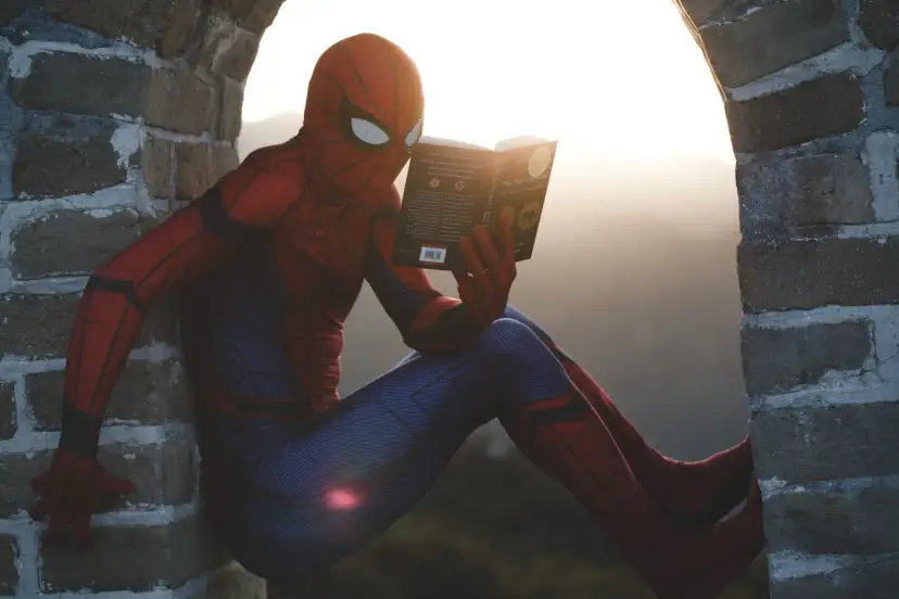 Spider-Man w czerwonym stroju siedzi na murze i czyta książkę. Czy komiks to utwór literacki? Nawet superbohaterowie potrzebują chwili wytchnienia i wiedzy.