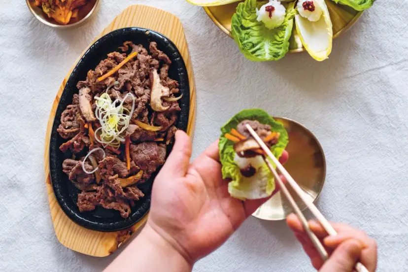 Pyszne bulgogi przepis na talerzu. Ktoś właśnie przygotowuje idealny kęs w liściu sałaty.