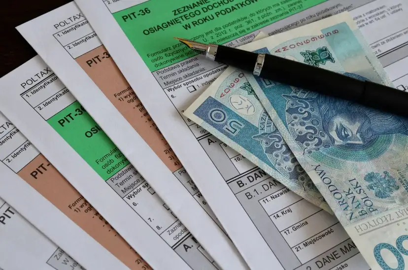 Formularze PIT, długopis i polskie banknoty. Miesięczna kwota wolna od podatku jest ważnym elementem rozliczeń.