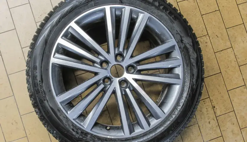 Felga aluminiowa z oponą zimową na tle kafelków.