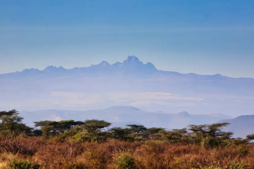 Widok na majestatyczny najwyższy szczyt Kenii, Batian, wyłaniający się z mgły nad sawanną.