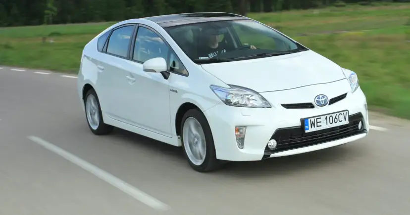 Biała Toyota Prius w ruchu. Czy warto kupić ten hybrydowy samochód?