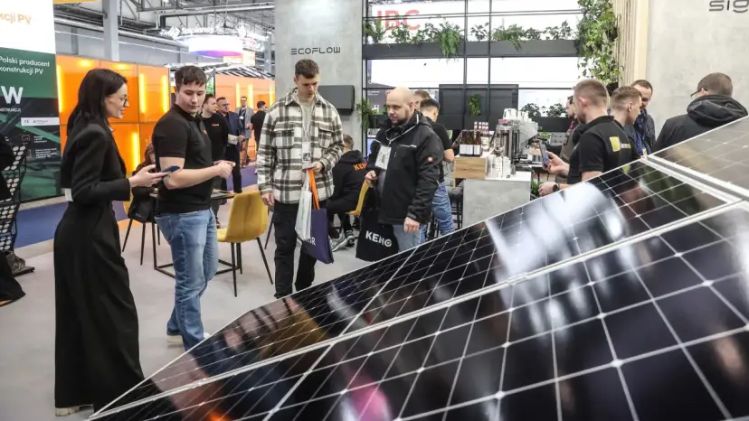 Ludzie zwiedzają targi energii odnawialnej, oglądając panele słoneczne i stoiska firm.