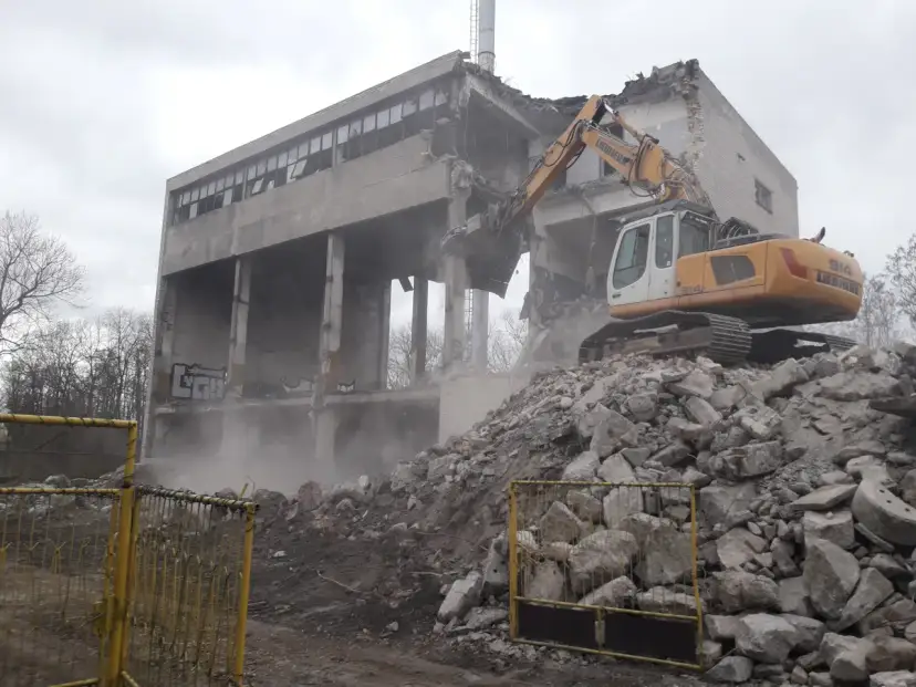 Żółty koparka rozbiórkowa pracuje przy burzeniu budynku. Widać stertę gruzu i kurz. Szukasz informacji o firmy rozbiórkowe cennik?