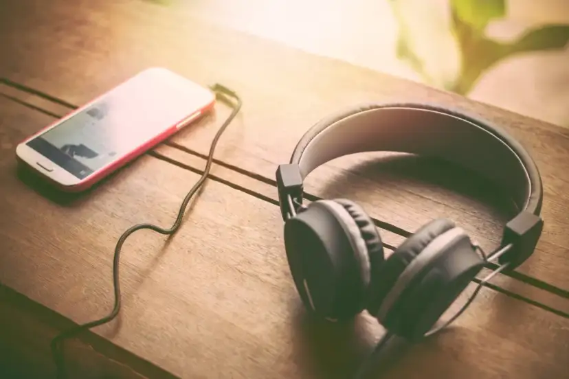 Słuchawki i smartfon leżące na drewnianym stole.