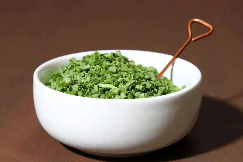 Misternie posiekany szczypiorek w białej miseczce, gotowy do tego, by go suszyć czy mrozić.