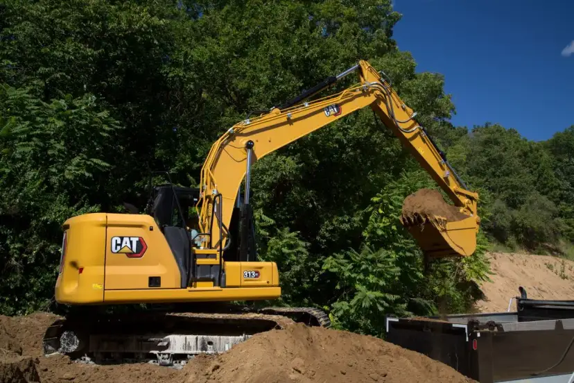 Żółta koparka Cat 313 z łyżką pełną ziemi, gotowa do pracy. Dane techniczne tej maszyny budowlanej są imponujące.