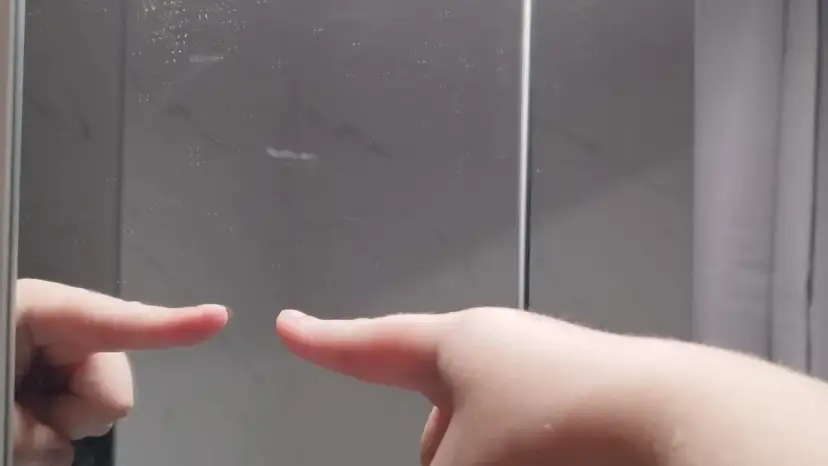 Palec wskazujący dotyka lustra, sprawdzając, jak sprawdzić czy lustro jest weneckie. Po drugiej stronie widać odbicie.