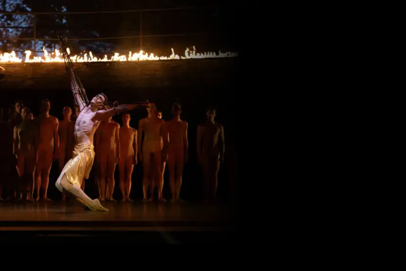 Tancerz w złotej spódnicy, z ogniem nad głową, symbolizuje, dlaczego Prometeusz ukradł ogień. W tle stoją inni tancerze.