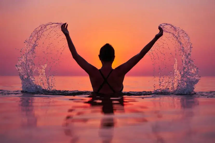 Kobieta w wodzie podczas zachodu słońca rozrzuca wodę, tworząc efektowne rozpryski. Czy Bałtyk jest czysty? Ta scena sugeruje, że tak.