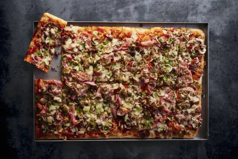 Pyszna pizza domowa przepis na blachę z szynką, pieczarkami i oliwkami. Idealna na rodzinne spotkanie.