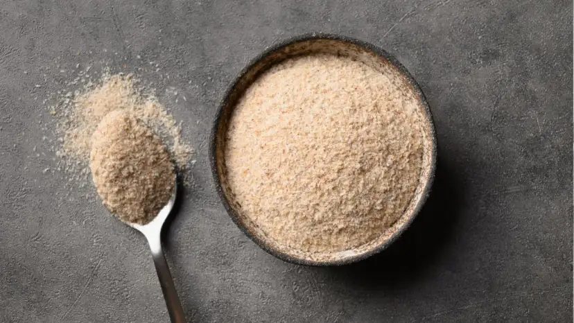 Łyżka i miska pełne jasnego proszku, który jest błonnikiem rozpuszczalnym w wodzie.