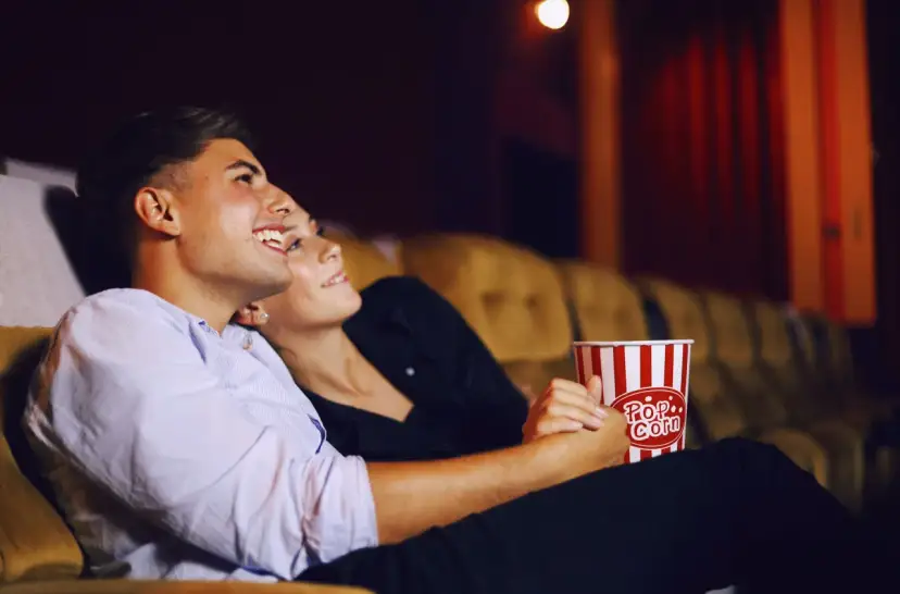 Para randkę do kina wybierz wygodny, ale stylowy strój. Para siedzi blisko siebie, trzymając popcorn.