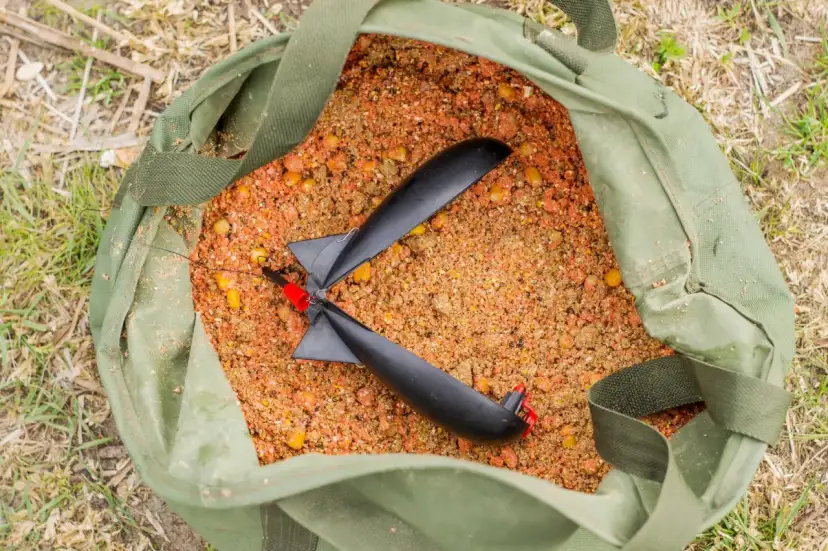 Gotowy do łowienia karpi? Oto jak zrobić zanętę na karpia: mieszanka ziaren i kukurydzy w zielonej torbie z dwoma czarnymi rakietami zanętowymi.