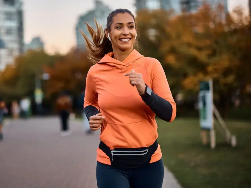 Kobieta w pomarańczowej bluzie biega w parku jesienią.