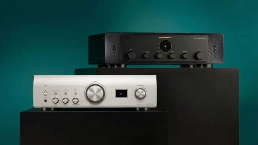 Dwa amplitunery: srebrny Denon i czarny Marantz, ustawione na czarnych podstawkach.