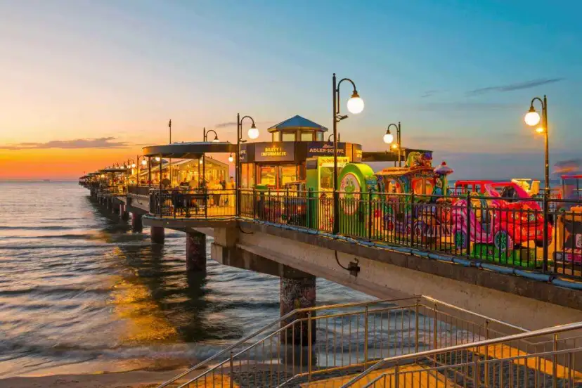 Molo w Międzyzdrojach o zachodzie słońca, z kolorowymi karuzelami i restauracjami. Idealne miejsce, by zobaczyć, co zwiedzić w Międzyzdrojach.