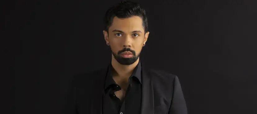 Mężczyzna w czarnym garniturze, z zarostem i kolczykiem w uchu. Jego spojrzenie sugeruje, że posiada najwyższy głos męski.