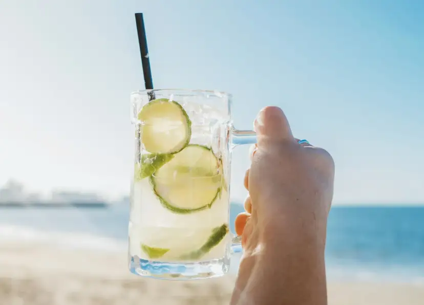 Orzeźwiająca Caipirinha czy Caipiroska z limonką i lodem w dłoni na tle plaży i morza. Idealny napój na upalny dzień.