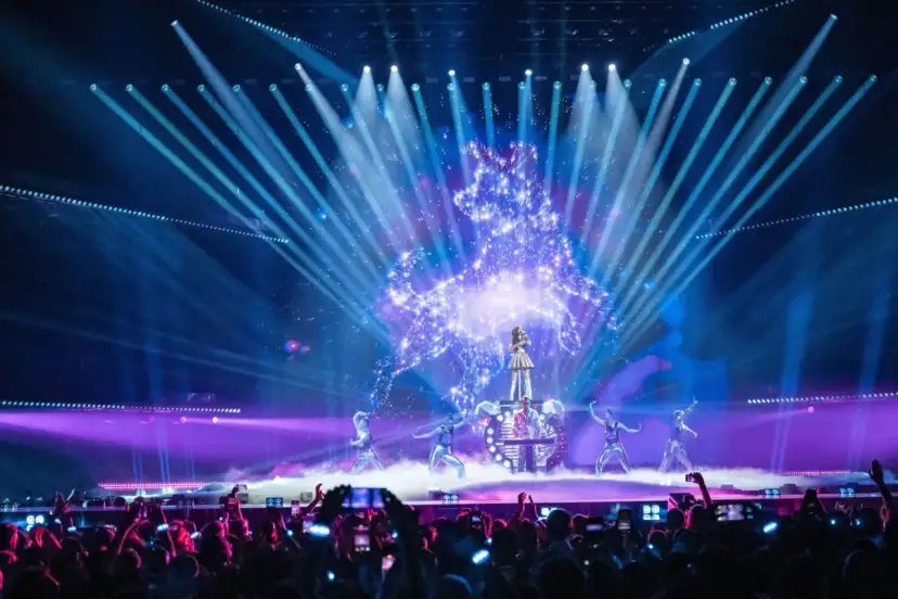 Wokalistka na scenie Eurowizji, otoczona tancerzami i efektami świetlnymi. Widownia filmuje występ, zastanawiając się, ile krajów w finale Eurowizji.