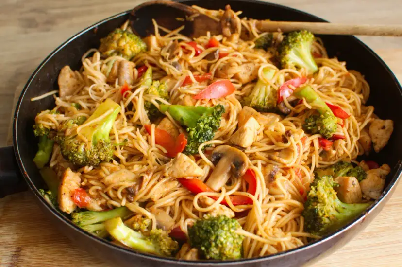 Pyszny makaron z kurczakiem po azjatycku z brokułami i pieczarkami w sosie, podany w woku.
