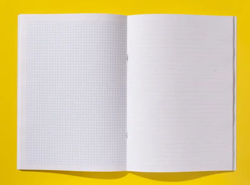 Otwarty zeszyt z kartkami w kratkę i w linie na żółtym tle.