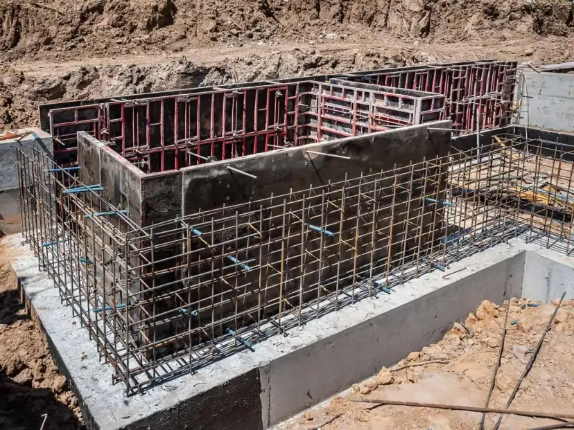 Siatka zbrojeniowa otacza betonowe szalunki, tworząc solidne zbrojenie ściany fundamentowej.