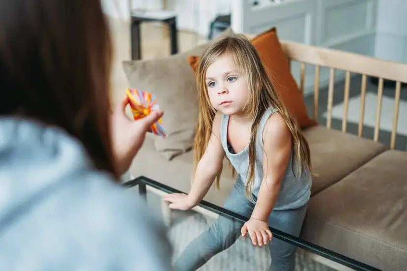 Dziewczynka z uwagą patrzy na kolorową zabawkę trzymaną przez mamę. Czy afazja u dzieci jest wyleczalna? Terapia może pomóc.