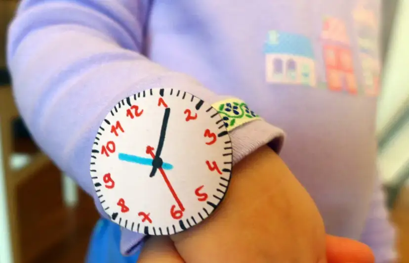 Jak zrobić wskazówki do zegara z papieru? Dziecko nosi na ręce własnoręcznie zrobiony zegarek z papieru.