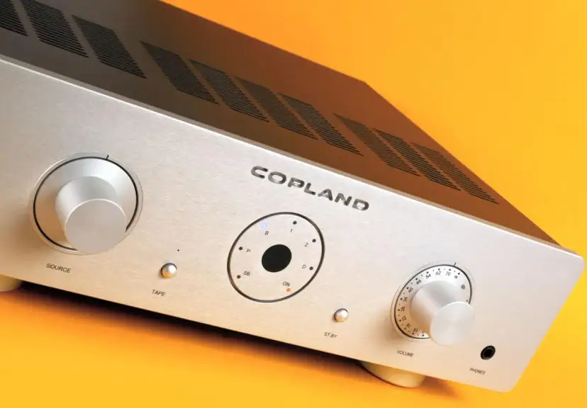 Srebrny wzmacniacz Copland CSA 100 z pokrętłami Source i Volume, przyciskiem Tape oraz wskaźnikami.