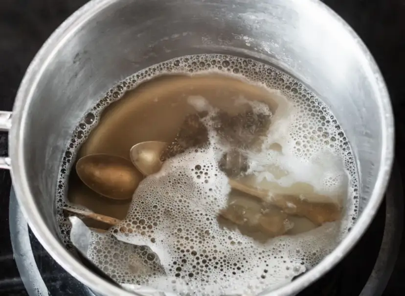 Srebrne łyżki i folia aluminiowa w garnku z bulgoczącą wodą.