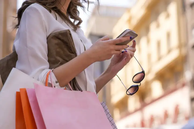 Kobieta z zakupami sprawdza telefon, planując refinansowanie pożyczki.