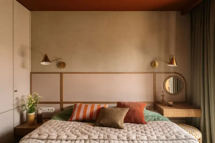 Przytulna sypialnia z łóżkiem, ozdobnymi poduszkami, lampkami i toaletką.