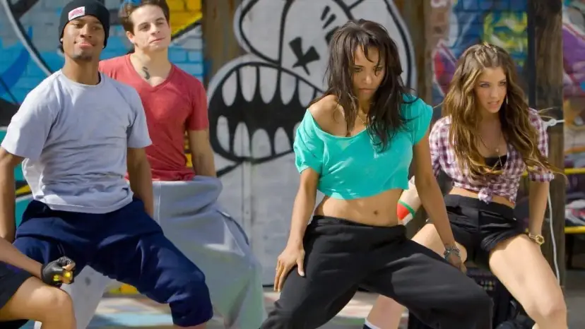 Grupa młodych ludzi w luźnych ubraniach tańczy na tle graffiti. Scena jak z filmów o tańcu, pełna energii i młodzieńczego buntu.