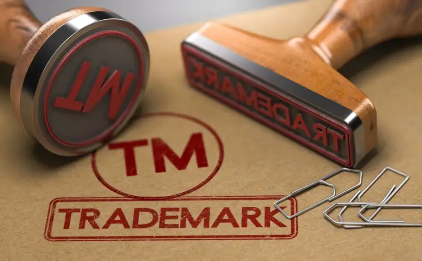 Dwa stemple z napisem "TRADEMARK" i symbolem "TM" na brązowym tle, obok spinaczy.