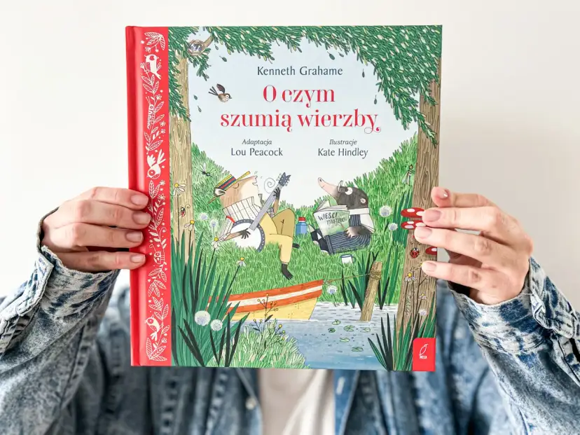 Okładka książki "O czym szumią wierzby" przedstawia zwierzątka nad rzeką. Kret czyta gazetę, a szczur gra na banjo.