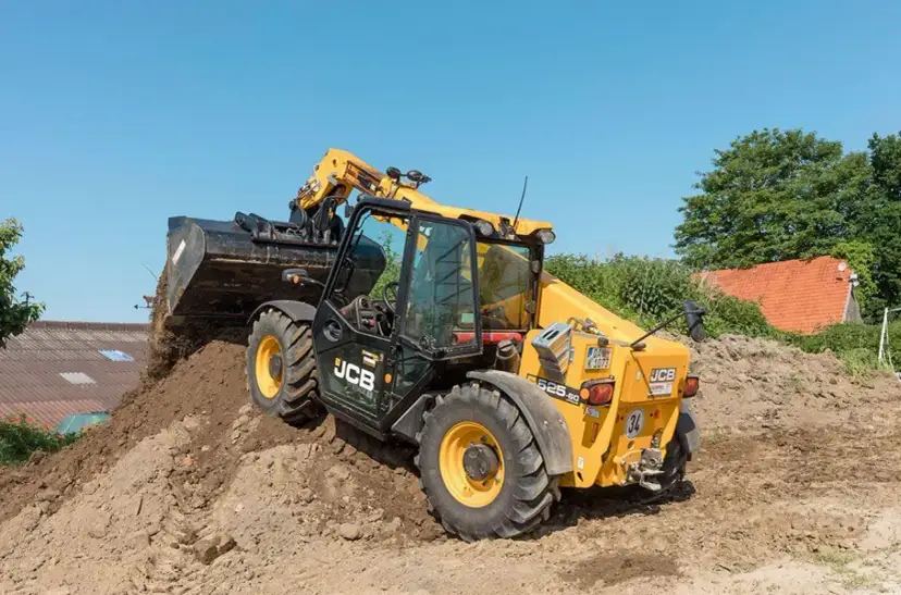 Żółty ładowarka teleskopowa JCB 525-60 z podniesionym wysięgnikiem i łyżką, pracująca na budowie.