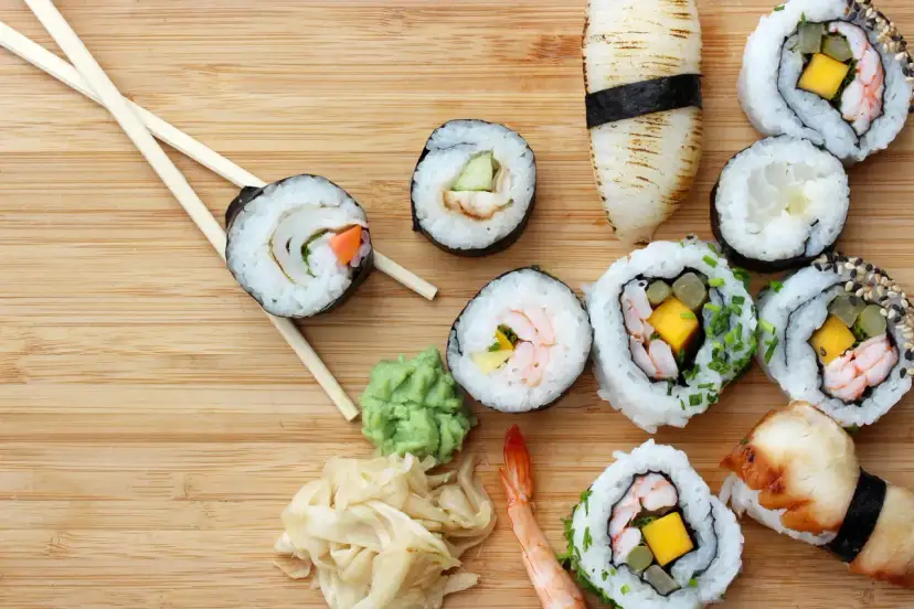 Różnorodne sushi z krewetkami, mango i warzywami, pałeczki, wasabi i marynowany imbir na drewnianym tle.