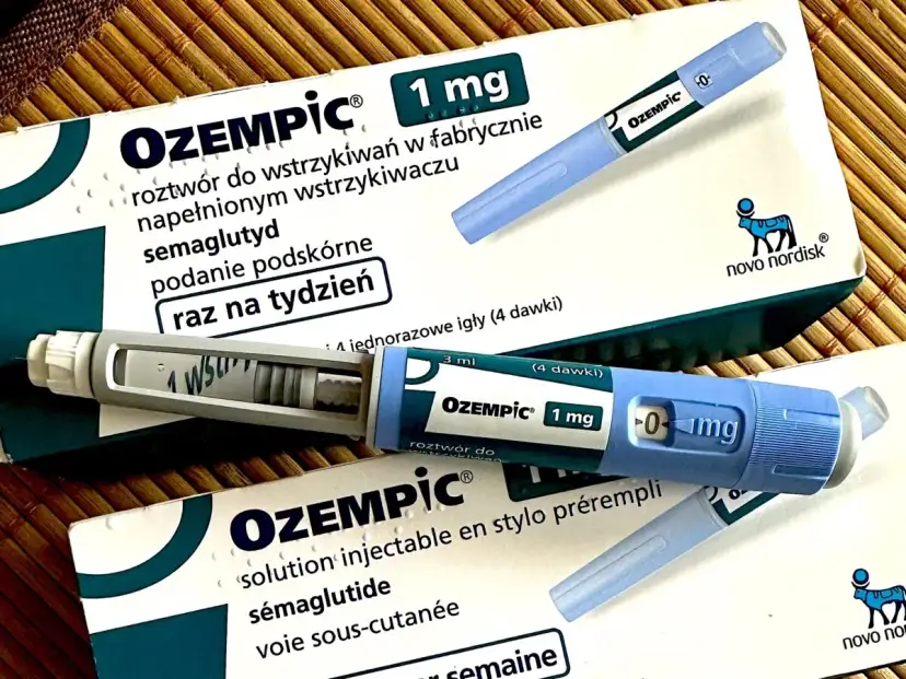 Dwa opakowania i dwa peny leku Ozempic 1 mg na podkładce bambusowej.