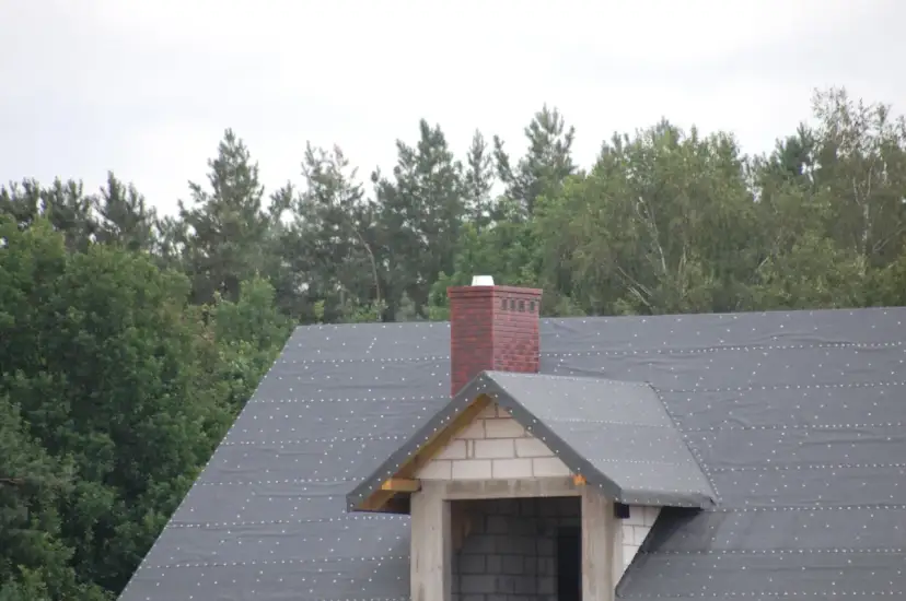 Ceglany komin na dachu w trakcie budowy. Zastanawiasz się, jak naprawić pęknięty komin? Ten obraz pokazuje jego obecny stan.