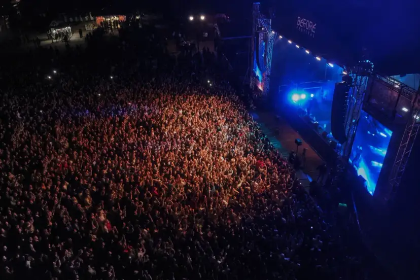 Tłum ludzi na koncercie, rozświetlony sceną i światłami. Atmosfera przed festiwalem Before Festival jest elektryzująca.