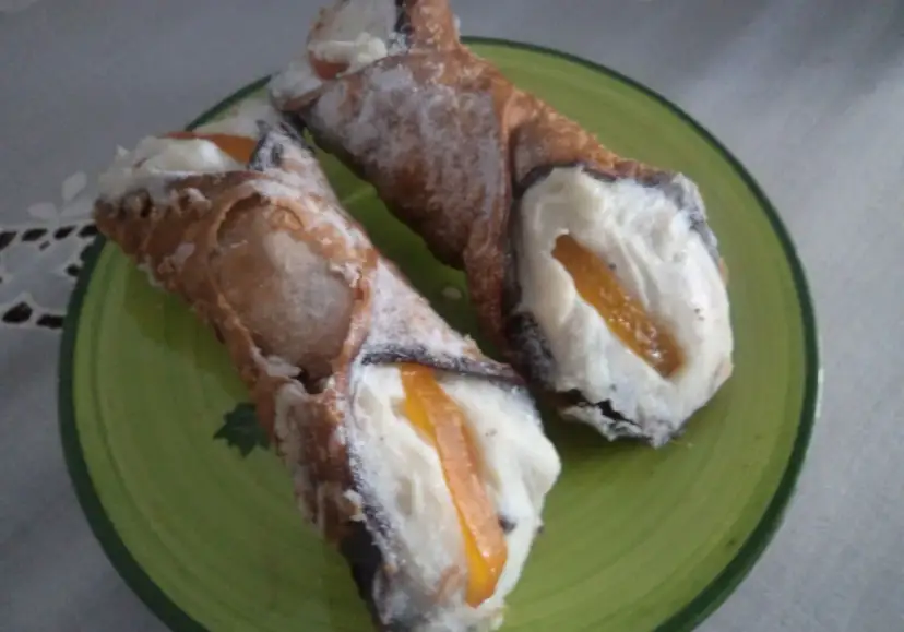 Dwa pyszne cannoli z kremem i kandyzowaną skórką pomarańczową, posypane cukrem pudrem. Ten makaron to prawdziwa rozkosz!
