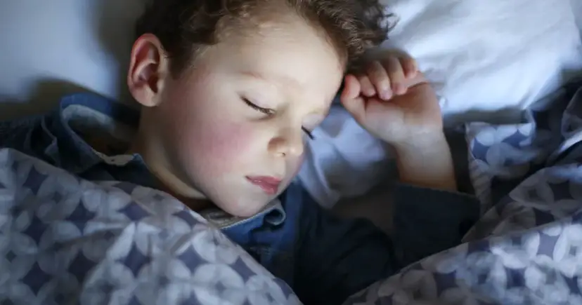 Mały chłopiec śpi pod kołdrą. Może nawet mówi przez sen, opowiadając o swoich snach.