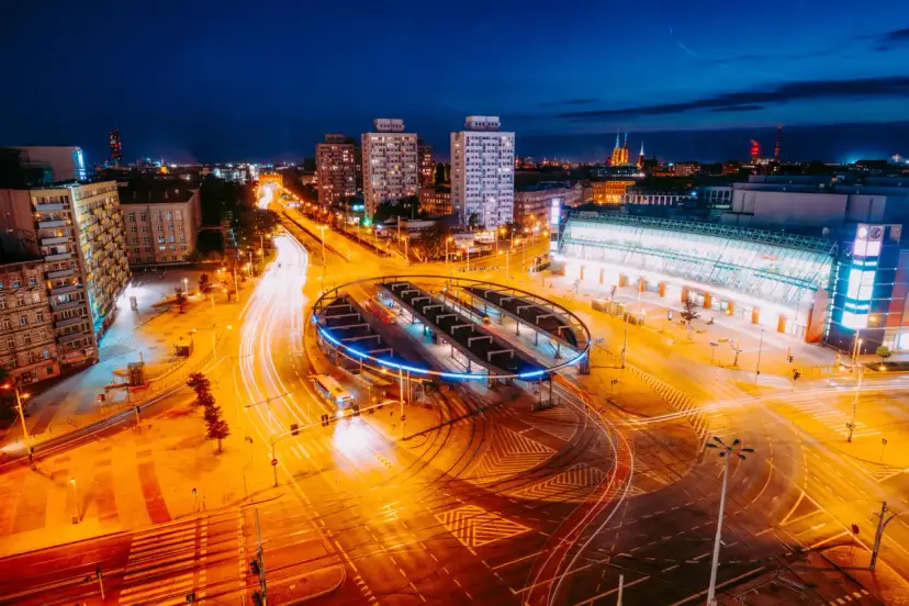 Widok z lotu ptaka na nocne miasto z długimi smugami świateł samochodowych i tramwajowych.