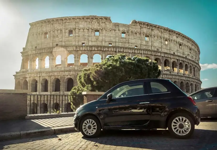 Czarny Fiat 500 pod Koloseum w Rzymie. Zastanawiasz się, ile się jedzie z Polski do Włoch samochodem?