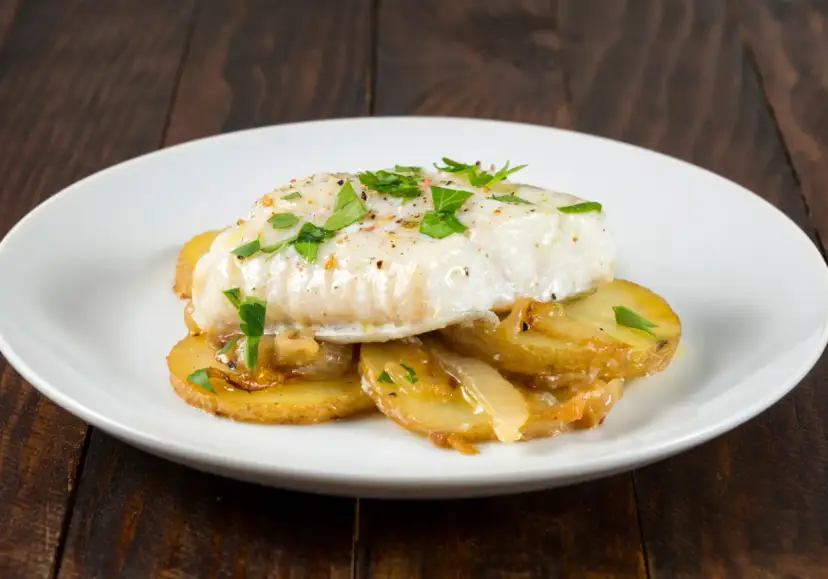 Pieczony filet z dorsza na plastrach ziemniaków, posypany natką pietruszki.