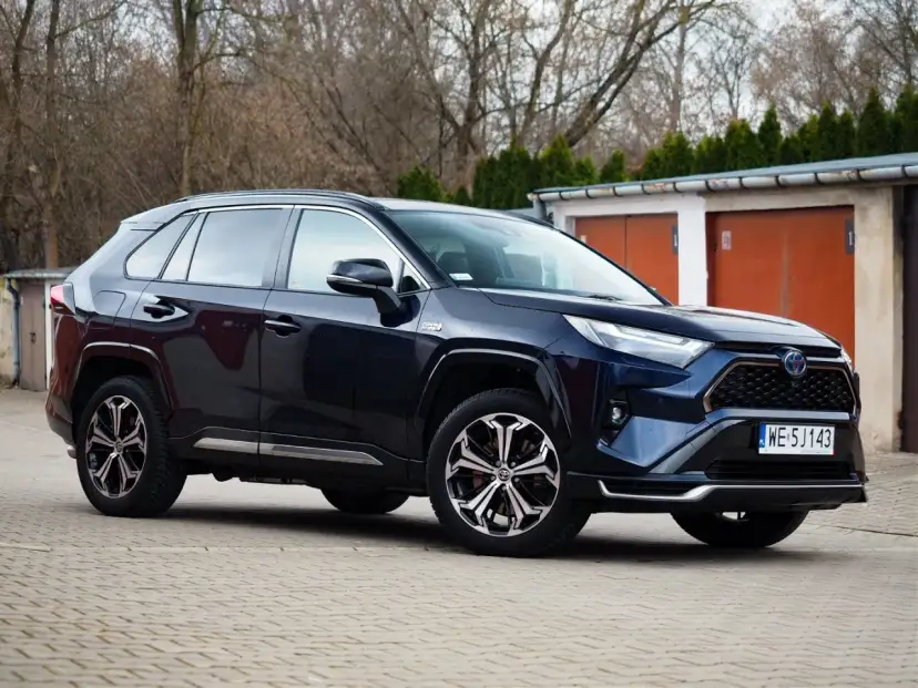 Ciemnoniebieski Toyota RAV4 Hybrid zaparkowany przed garażami.