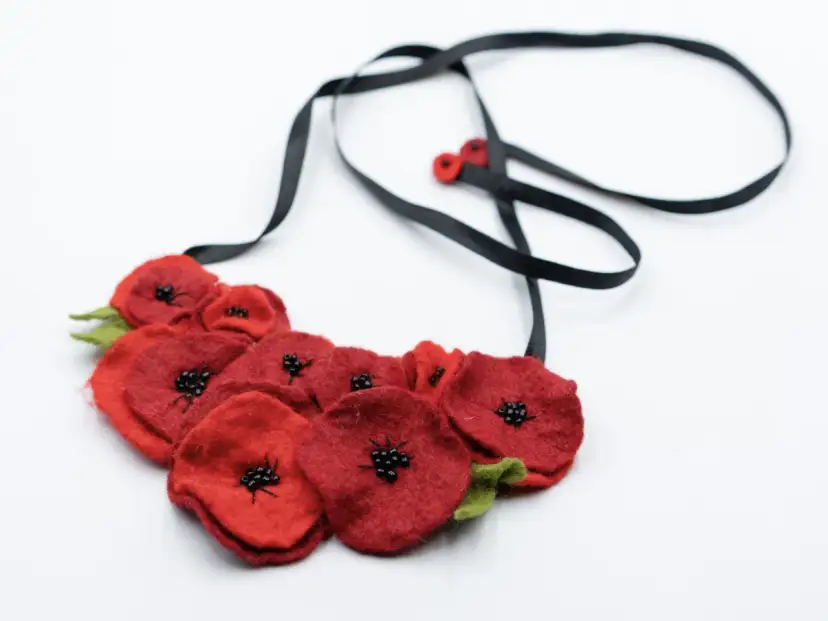 Naszyjnik z filcu w kształcie czerwonych maków z czarnymi koralikami w środku i zielonymi listkami.